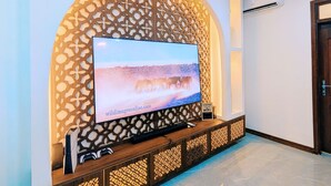 A modern living room with a large flat-screen TV mounted on a decorative wall, a wooden entertainment unit below, and a tiled floor. - ZAURA ZANZIBAR (Zanzibar Town)