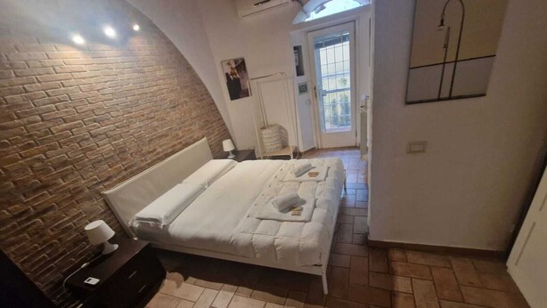 Une chambre avec un mur en briques, un lit avec une literie blanche, une table de chevet et une lampe.