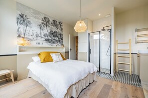 Ein Schlafzimmer mit Bett, Nachttisch, Pendelleuchte, Duschbereich und Badezimmer mit Waschbecken und Handtuchhalter.