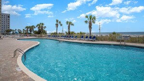 Une piscine à l’eau bleue, entourée de palmiers et de chaises longues.