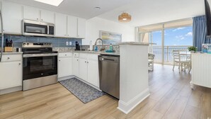 Une cuisine moderne avec des meubles blancs, des appareils en acier inoxydable et une grande fenêtre donnant sur un balcon.