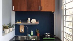 A compact kitchen with wooden cabinets, a stainless steel sink, and a window with blinds. - The Vinh Homestay (Ho Chi Minh City)