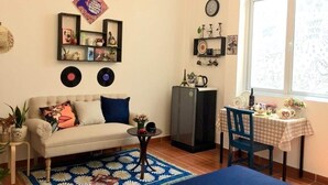 A cozy living room with a sofa, a small table, a refrigerator, and a window with a view. - The Vinh Homestay (Ho Chi Minh City)