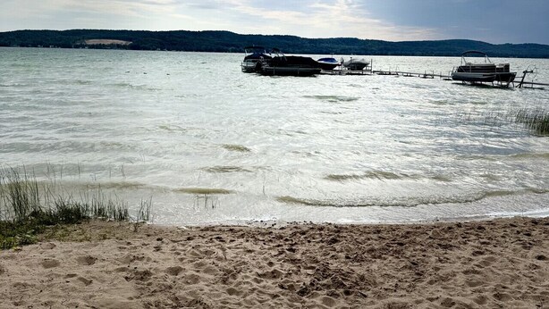 A beach with boats docked, a sandy shore, and a distant hilly landscape under a cloudy sky.