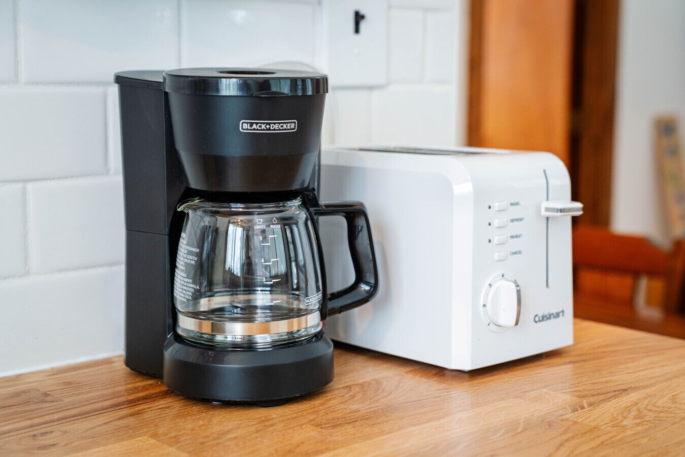 A black and white coffee maker with a glass carafe and a white toaster on a wooden table.