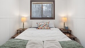 A bedroom with a large bed, two bedside tables, a window with a view of trees, and two lamps.