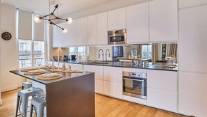A modern kitchen with white cabinets, stainless steel appliances, and a central island with stools. - Superb apartment Center of Paris Le Marais (Paris)