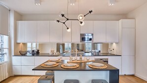 A modern kitchen with white cabinets, a central island with stools, a stainless steel oven, and a unique chandelier. - Superb apartment Center of Paris Le Marais (Paris)