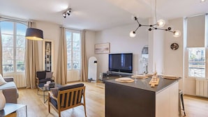 A modern living room with a TV, seating, and a dining area with a central island. - Superb apartment Center of Paris Le Marais (Paris)