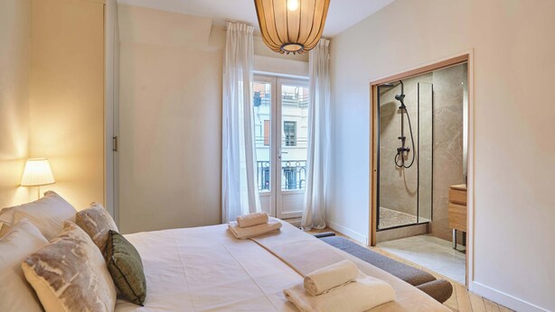 A hotel room with a large bed, a bedside lamp, a shower area, and a view of the outside balcony. - Superb Apartment Terrace Champs Elysees (Paris)
