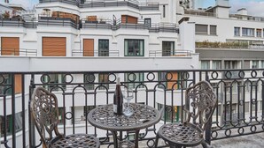 A balcony with a round table and two chairs, overlooking a modern building with balconies. - Superb Apartment Terrace Champs Elysees (Paris)