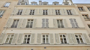A multi-story building with white shutters, a balcony on the second floor, and a sign indicating the address. - Luxurious AC Apartment Louvre Museum Saint Honoré (Paris)