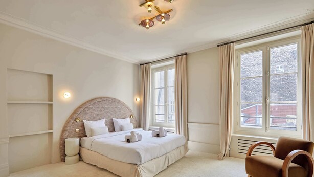 A bedroom with a large bed, a wooden chair, and a window with curtains. - Luxurious AC Apartment Louvre Museum Saint Honoré (Paris)