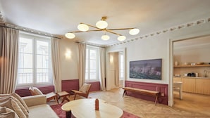 A spacious living room with a large window, a wooden coffee table, a sofa, and a television. - Luxurious AC Apartment Louvre Museum Saint Honoré (Paris)