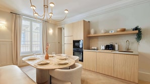 A modern kitchen with wooden cabinets, a built-in oven, and a countertop with a coffee maker and other appliances. - Luxurious AC Apartment Louvre Museum Saint Honoré (Paris)