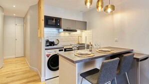 Una cucina moderna con forno integrato, microonde e lavatrice, un'area bar con sgabelli e illuminazione a sospensione.