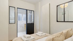 Una camera da letto moderna con un letto, un grande specchio e una porta scorrevole che dà su un bagno.