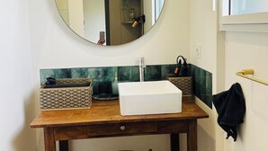 Un baño con tocador de madera, un lavamanos blanco, un espejo redondo y un toallero colgante.