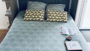 Una cama bien hecha con ropa de cama estampada, una mesita de noche con un libro y una taza, y una estantería con objetos decorativos.