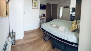 Un dormitorio con cama, un escritorio con silla, un espejo y un televisor en la pared.