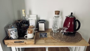 Mostrador de bar de madera con diversos objetos, incluyendo una cafetera, una botella de vidrio, una taza y una bandeja con un molinillo de café.