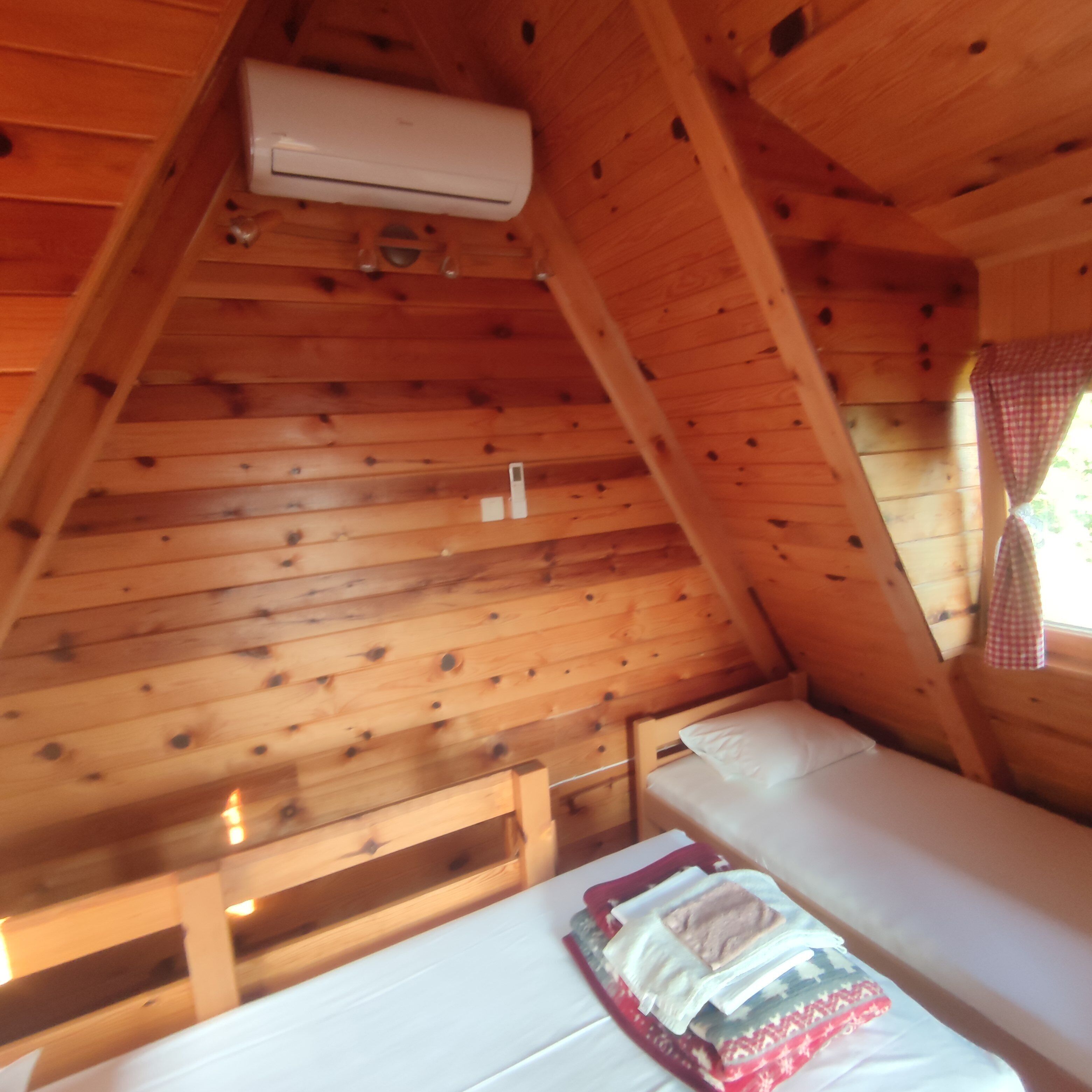 Ein Holzblockhaus-Innenraum mit Etagenbett, Deckenventilator und einem Fenster mit Karottenvorhängen.