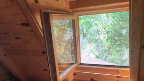 Habitación de cabaña de madera con una cama, una ventana y vistas al follaje exterior.