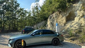 Un coche estacionado en una zona de grava, con un acantilado rocoso y árboles al fondo.