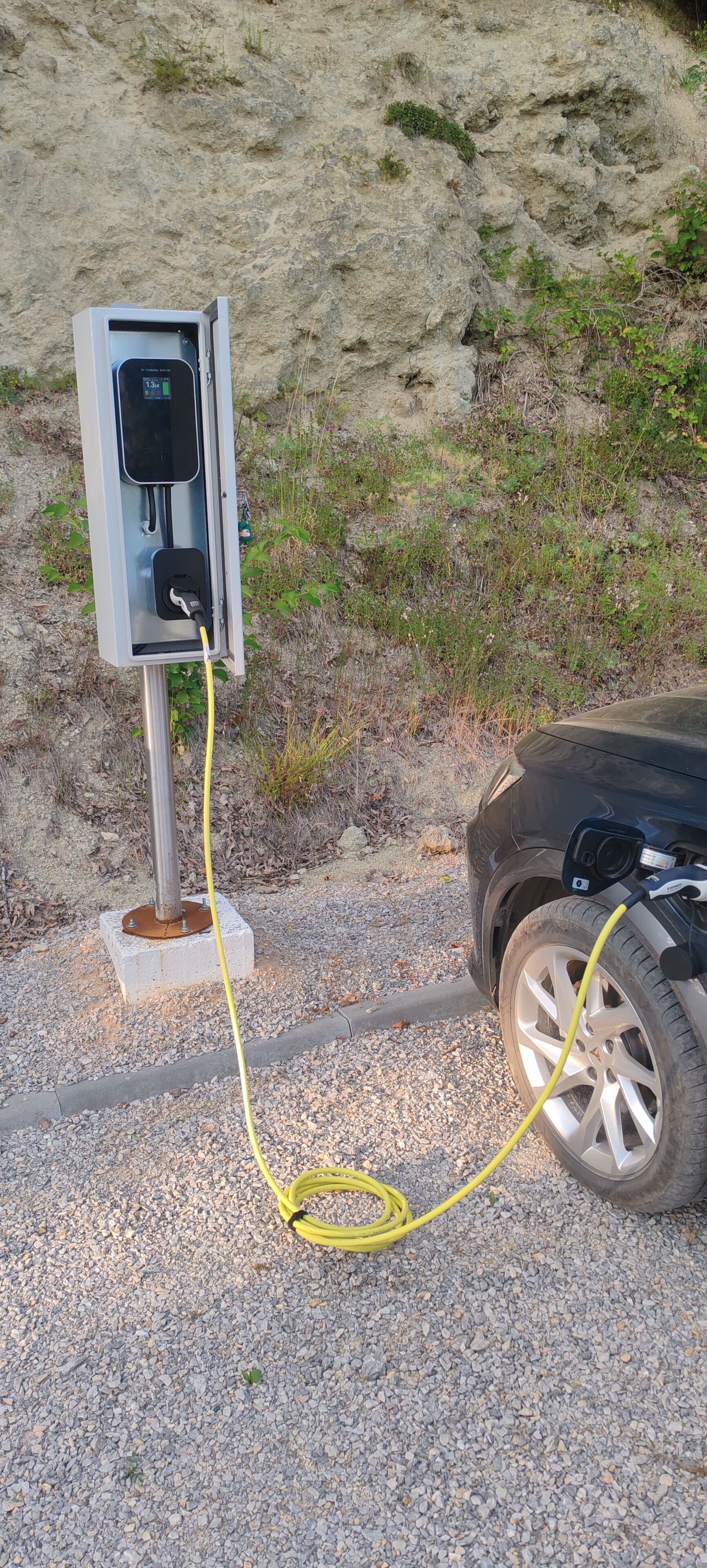 An electric vehicle charging station with a yellow cable connected to a car.