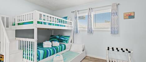 Habitación con literas, ventilador de techo, ventana con persianas y una pequeña alfombra.