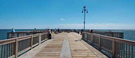 A wooden pier extending into the sea with people fishing and walking along it.