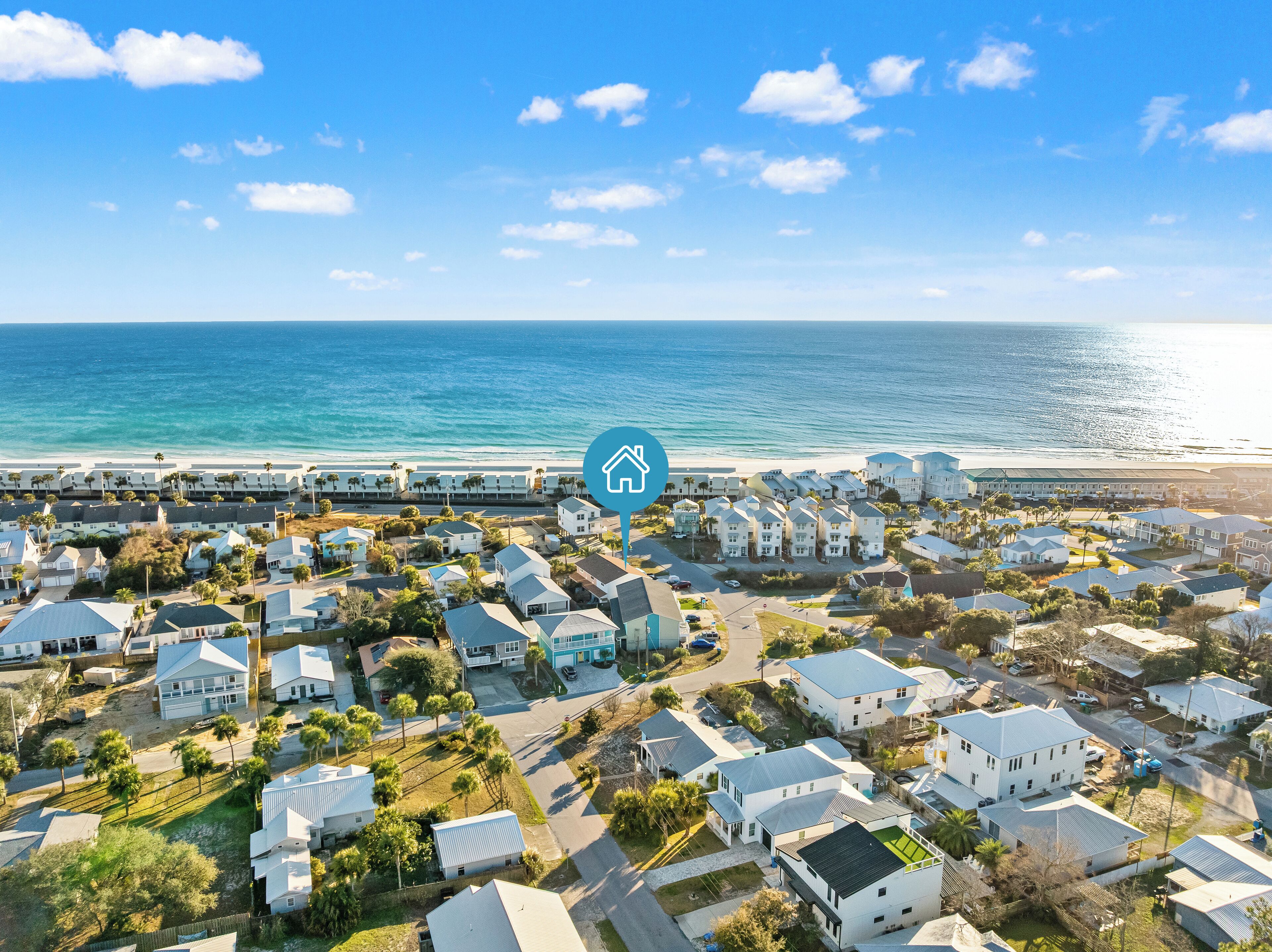 Vista aérea de una zona residencial costera con casas, una playa y un cielo despejado.