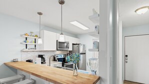 A modern kitchen with white cabinets, a wooden countertop, and stainless steel appliances. There are bar stools and a vase with flowers on the counter. - Stay at The Salty Palm! 2BR 1.5ba Sleeps 7 (Panama City Beach)
