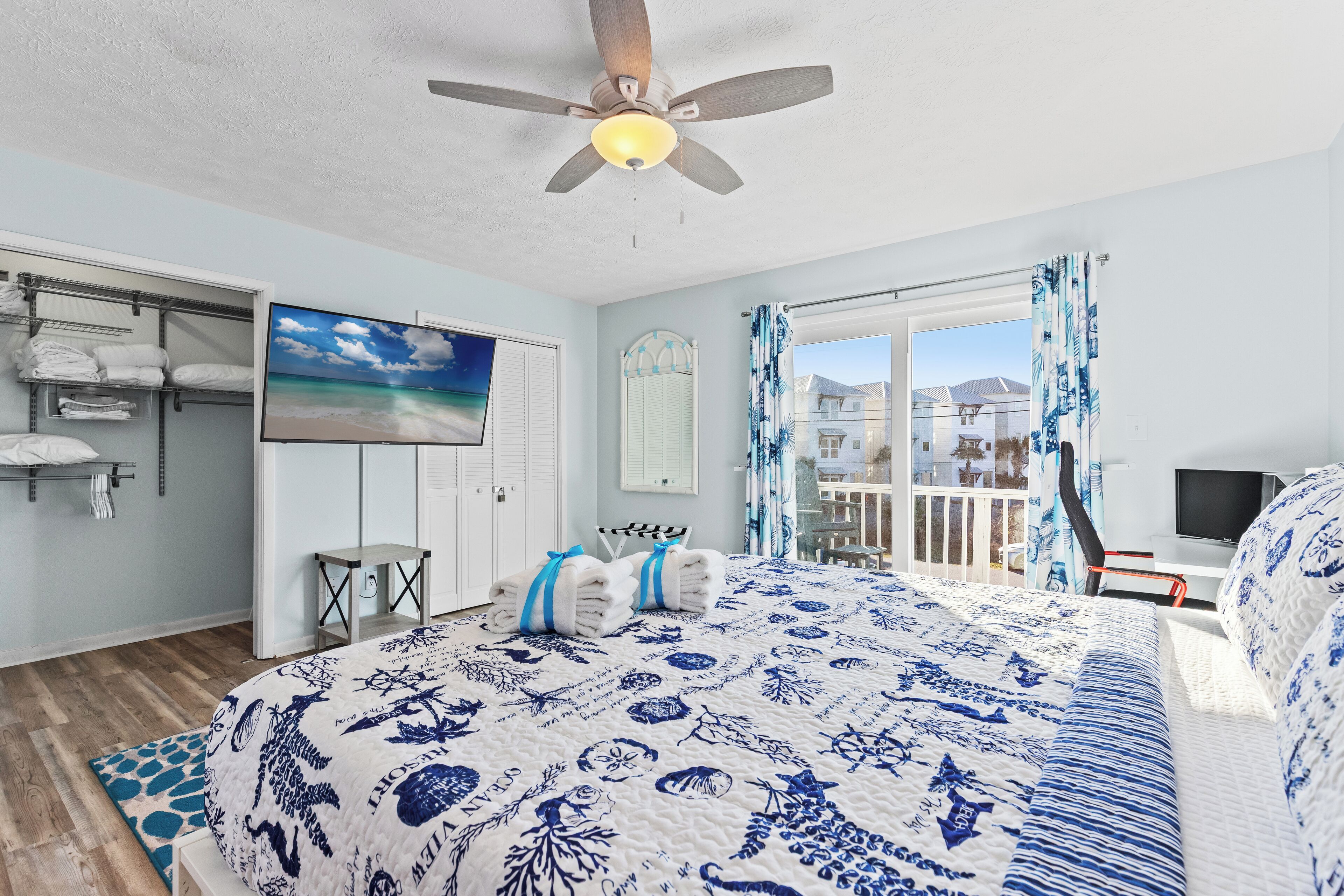 A bedroom with a bed, a ceiling fan, a TV, a balcony with a view, and a painting on the wall.