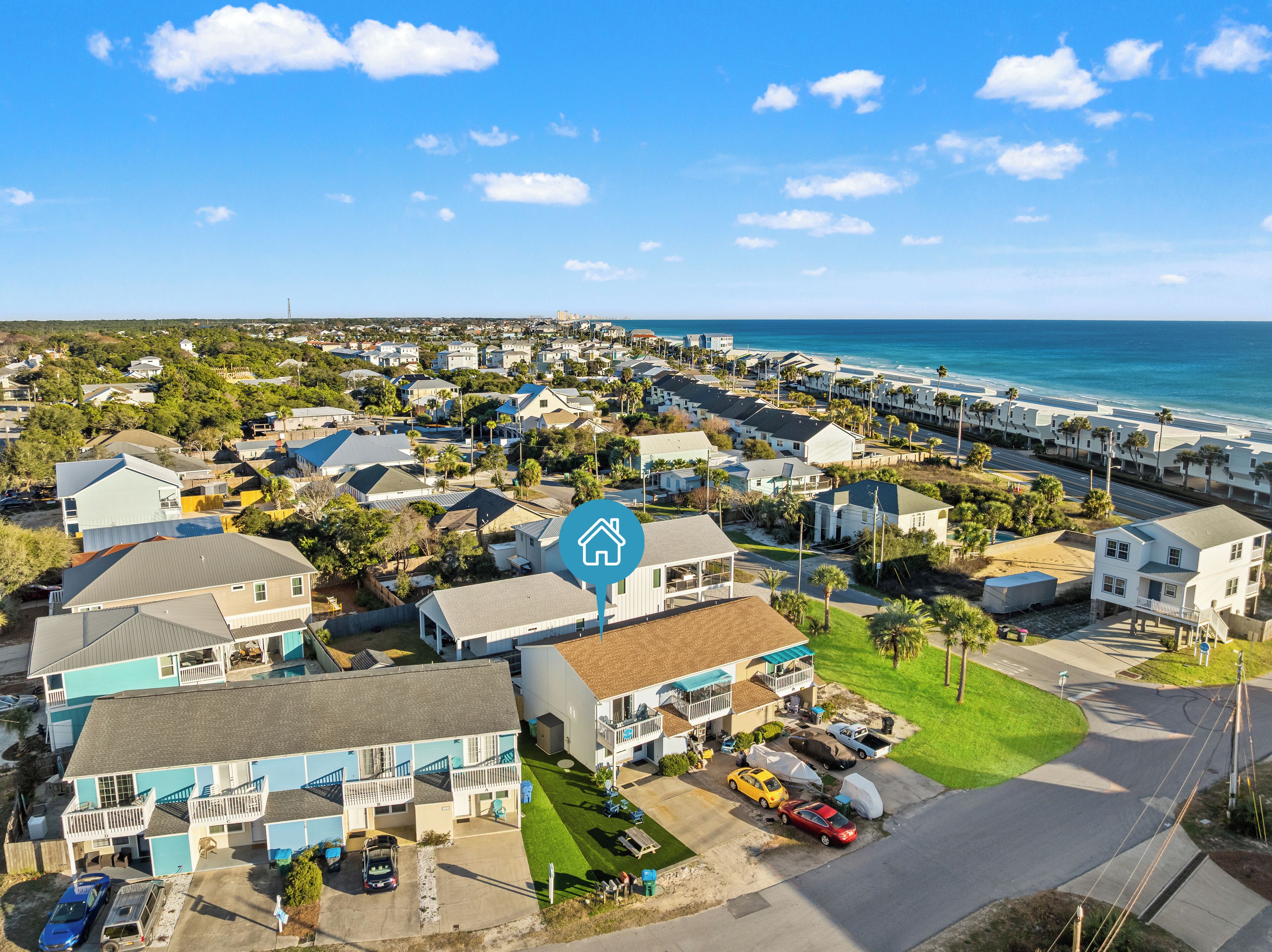 A coastal residential area with houses, a clear blue sky, and the ocean in the background.