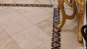 A hallway with a marble floor, a patterned carpet, and a golden ornate mirror.