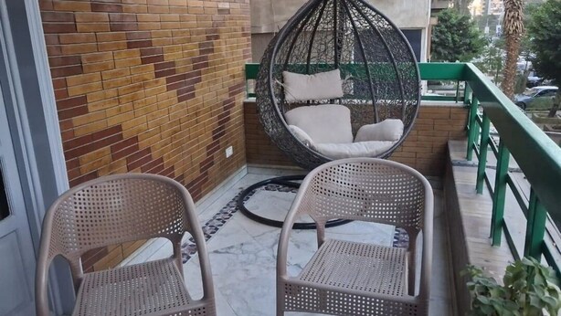 A balcony with two wicker chairs, a hanging chair, and a green railing.