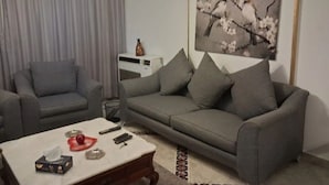 A living room with a grey sofa, a coffee table with remote controls, and a painting of a tree branch with flowers.