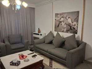 Un salón con un sofá gris, una mesa de centro con controles remotos y un cuadro de una rama de árbol con flores.