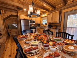 A wooden interior with a dining table set for a meal, kitchen appliances, and a large window. - Cabin at Walland Forest (Walland)