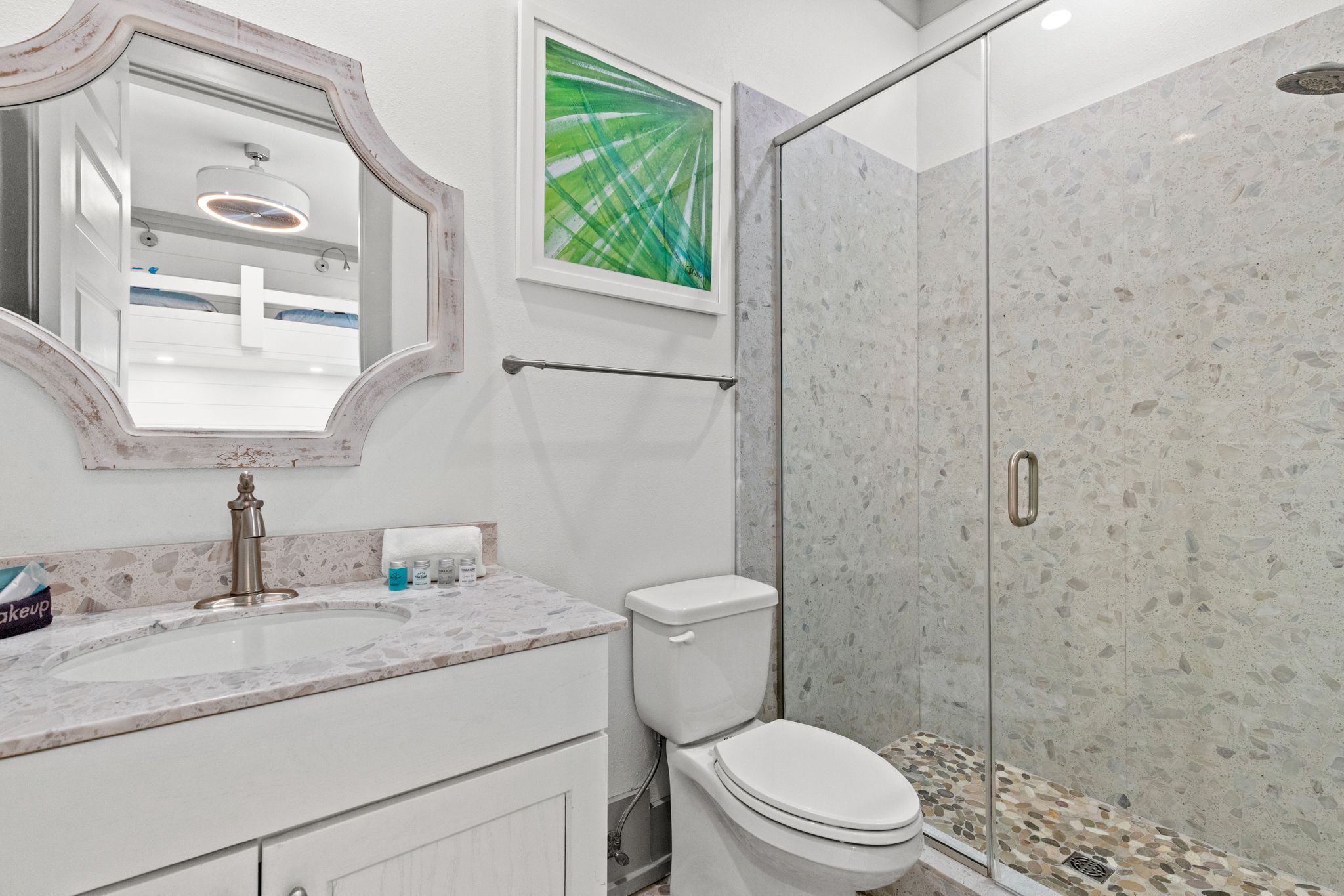 Ein Badezimmer mit Marmorwaschtisch, Toilette, einer Duschkabine aus Glas und einem gerahmten Bild an der Wand.