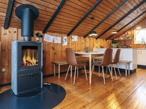 A cozy room with a wood-burning stove, wooden walls, a dining table with chairs, and a kitchen area. - 6 Person Holiday Home in Fjerritslev (Fjerritslev)