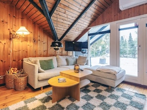 A cozy living room with a wooden ceiling, a sofa, a coffee table, and a view of a snowy landscape through a glass door. - 6 Person Holiday Home in Fjerritslev (Fjerritslev)