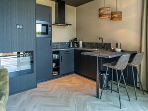 A modern kitchen with a built-in microwave, a stove, and a sink. There are two bar stools and a hanging light fixture. - Private Sauna at Wellness Lodge in Drenthe (Dalerveen)