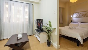 A hotel room with a bed, a TV on a stand, a potted plant, and a table with a towel. - Cozy 1-bedroom apartment in delightful Taguig with AC and gym access (Taguig)