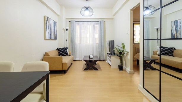 A modern living room with a sofa, a coffee table, and a dining table. - Cozy 1-bedroom apartment in delightful Taguig with AC and gym access (Taguig)
