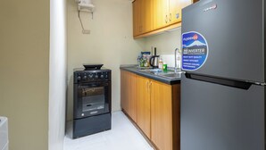 A compact kitchen with wooden cabinets, a black stove, and a refrigerator with a sticker. - Cozy 1-bedroom apartment in delightful Taguig with AC and gym access (Taguig)