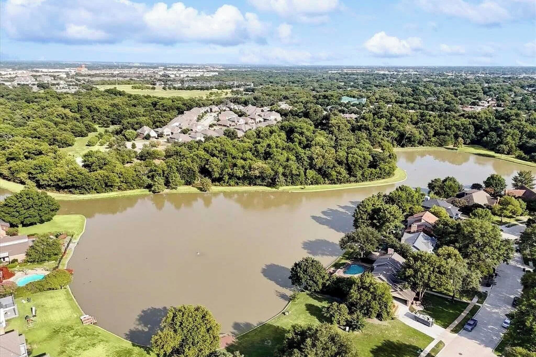 An aerial view of a residential area with a large pond, houses, and a golf course.