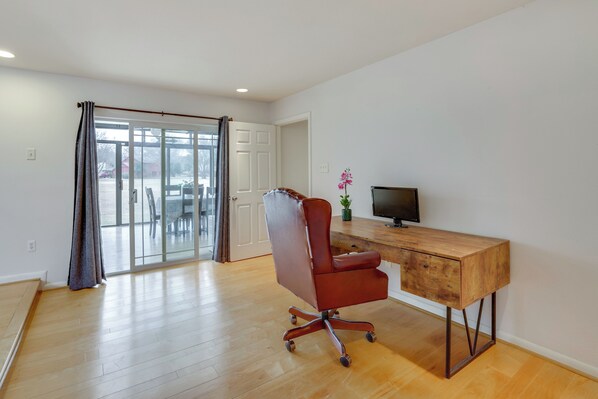 A spacious room with a wooden desk, a red office chair, a television, and a sliding glass door leading to an outdoor area.