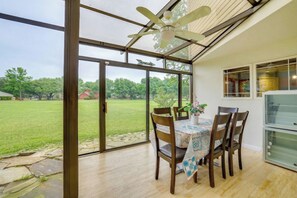 Un comedor con una mesa, sillas, ventilador de techo y vistas a un campo con árboles.